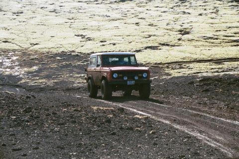 1974 Ford Bronco - A classic red Ford Bronco navigates a , off-road terrain with sparse vegetation.