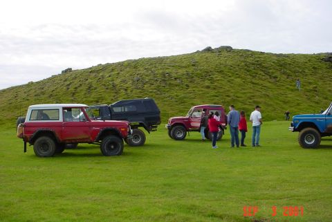 1974 Ford Bronco - Several SUVs are parked on a grassy hill under a cloudy sky.
