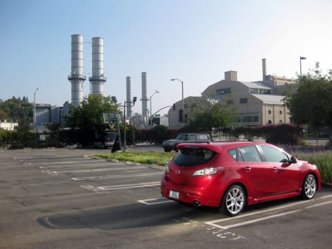 1989 Mazda MX-6 - A red hatchback is parked in a lot with a power plant in the background.