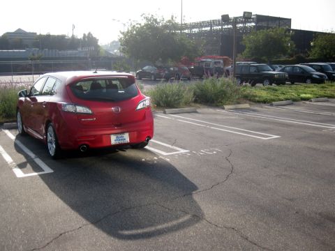 1989 Mazda MX-6 - Red Mazda 3 hatchback parked in a lot with other vehicles visible in the background.