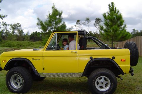 1974 Ford Bronco - A bright yellow 1974 Ford Bronco is seen from the side with a man and a child inside.
