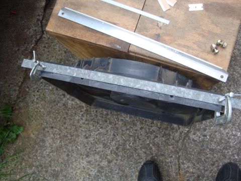 1989 Ford Bronco - A radiator fan assembly is secured with clamps and metal bars, resting on a wooden surface outdoors.