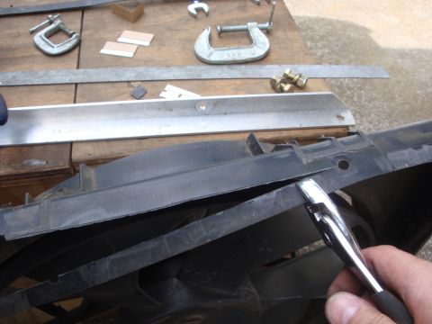 1989 Ford Bronco - A close-up view of a black plastic radiator fan shroud being worked on with a metal tool.