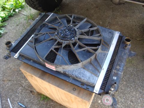 1989 Ford Bronco - A radiator and fan assembly is shown resting on a wooden block outdoors, with a tire visible in the background.