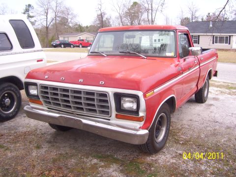1978 Ford Bronco - Red Ford F-Series pickup truck parked outside with a white camper shell on another truck nearby.