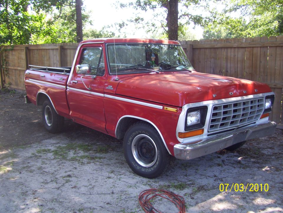 Red Ford pickup truck, 3/4 front view, parked by wooden fence