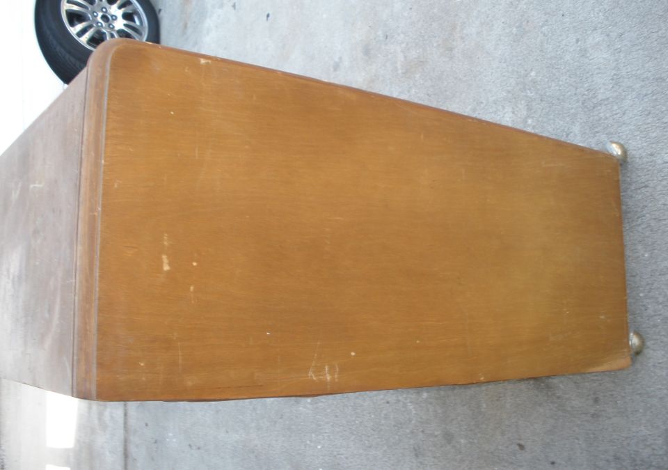 Side of a vintage wood dresser on driveway, alloy wheel in background