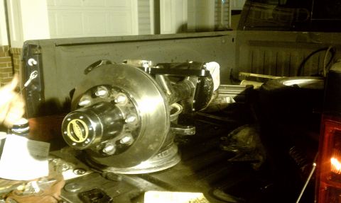 1990 Ford Bronco - Close-up of a front axle assembly with a disc brake rotor and hub, resting in the bed of a dark-colored truck.