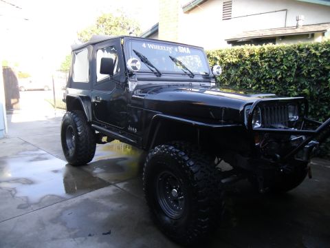 1992 Jeep Wrangler - This black Jeep Wrangler features large off-road tires and a custom front bumper, suggesting it's modified for off-roading.