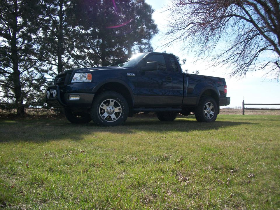 Dark blue pickup truck parked on grass with trees and a fence in the background