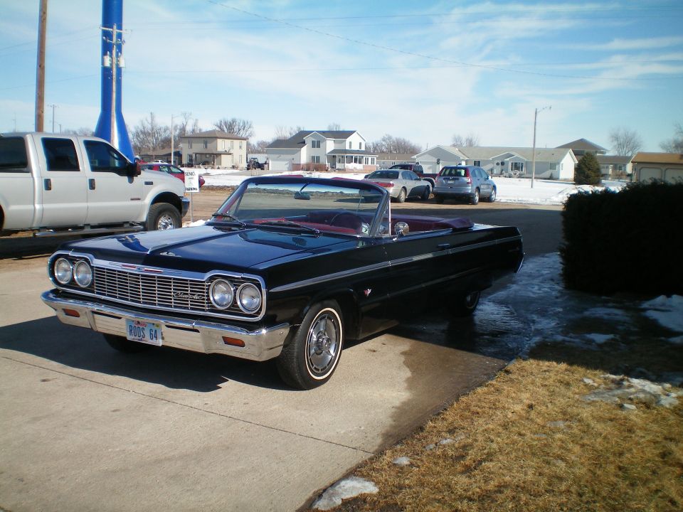 Black 1964 Chevrolet Impala convertible with a red interior, parked on a concrete driveway