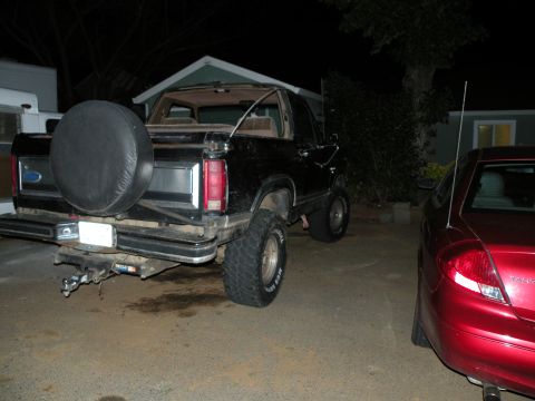 1986 Ford Bronco - Rear view of a black Ford Bronco parked next to a red sedan at night.