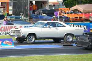 1966 Ford Fairlane - A white 1966 Ford Fairlane coupe is positioned on a drag strip, with other vehicles and spectators in the background.