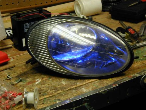 1998 Ford Taurus - A car headlight with a blue bulb sits on a workbench next to a battery and various tools.