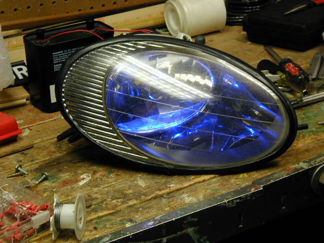 Headlight assembly with blue bulb on workbench with tools and battery