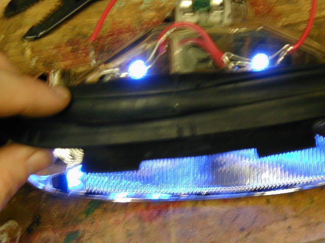 Blue LEDs glowing inside a clear lens light housing held over a workbench