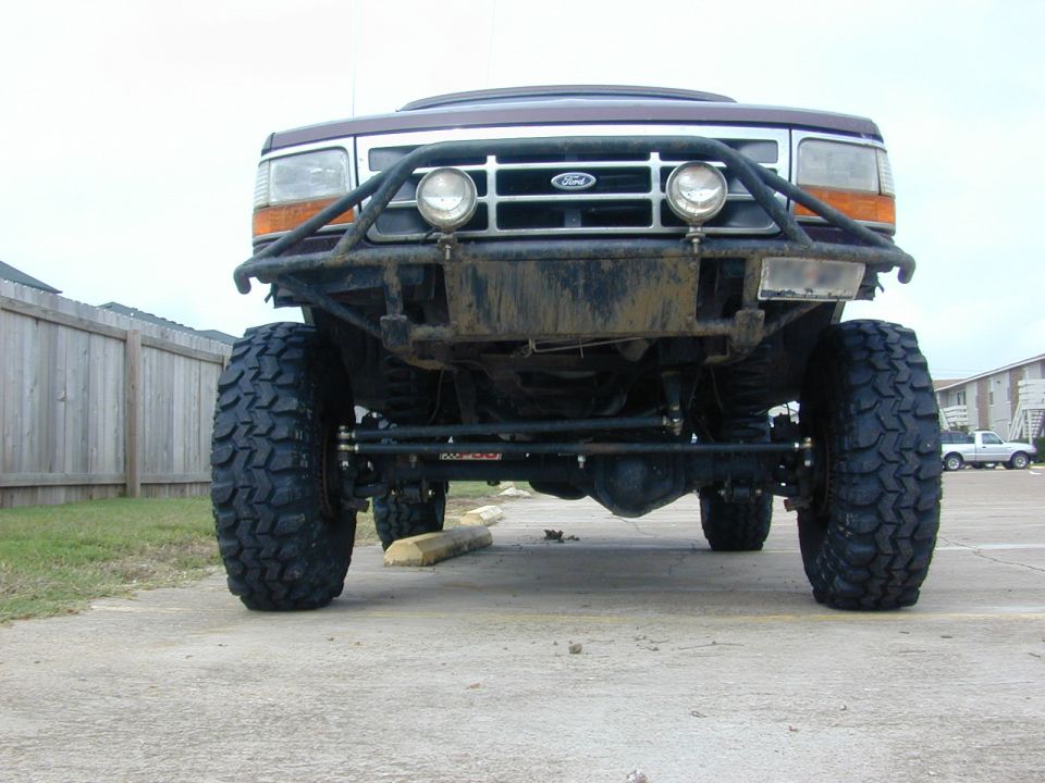 Front low view of lifted maroon Ford Bronco on big mud tires showing axle and tube bumper