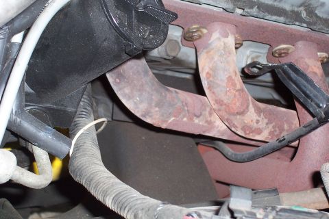 1988 Ford Bronco - This image shows a close-up view of a vehicle's exhaust manifold and associated wiring, with visible rust on the manifold.