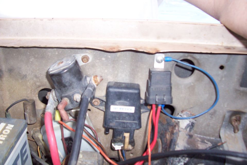 Close-up of starter solenoid, fuse box, and relays in a vehicle engine bay. Some wiring is visible