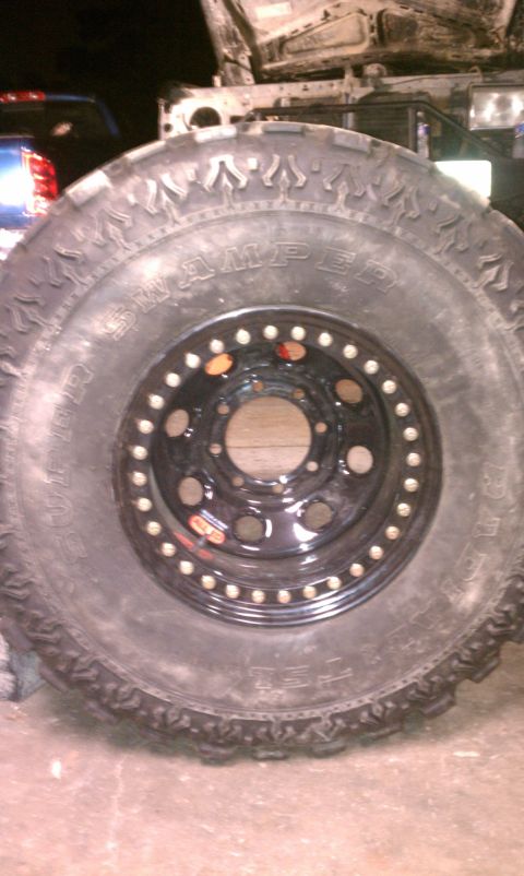 1990 Ford Bronco - A close-up of a large off-road tire and wheel assembly, with another vehicle visible in the background.