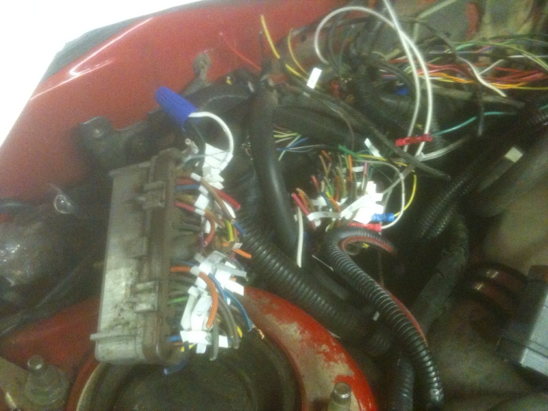 Engine wiring harness with a blue pen and a fuse box, red car body visible