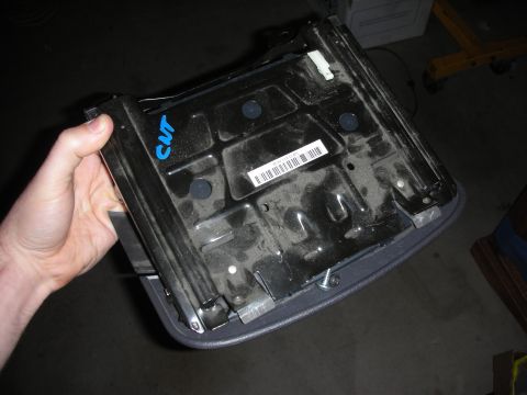 1998 Ford Crown Victoria - underside of a removed plastic center console held by hand, showing mounting points, a barcode sticker, and a blue handwritten CWT mark.