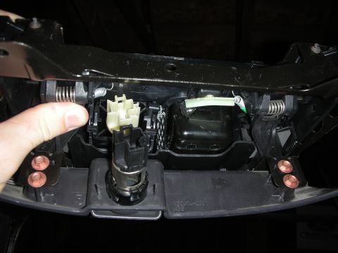 1998 Ford Crown Victoria - interior of a console base with coil springs, a white wiring connector, a lighter socket, and copper-toned bolt heads, pointed at by a fing…