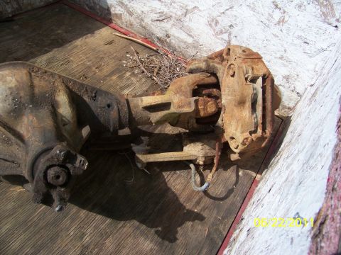 1989 Ford Bronco - A close-up view of a heavily rusted axle assembly, including a brake caliper, resting on a wooden surface.