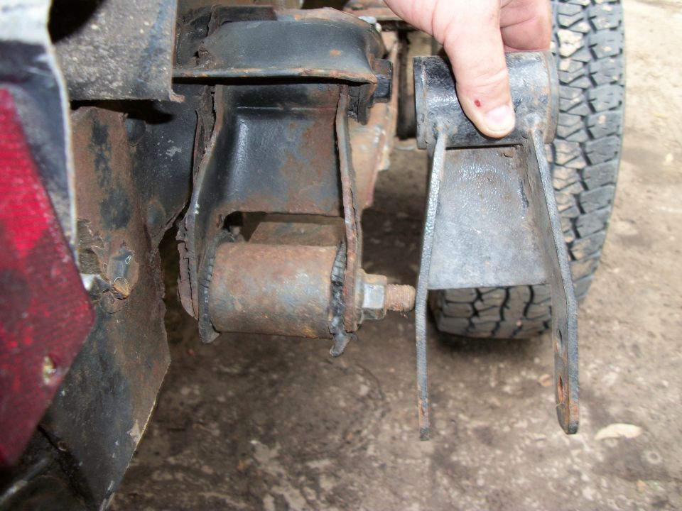 Rusted suspension bracket being held by a hand, with a tire visible in the background