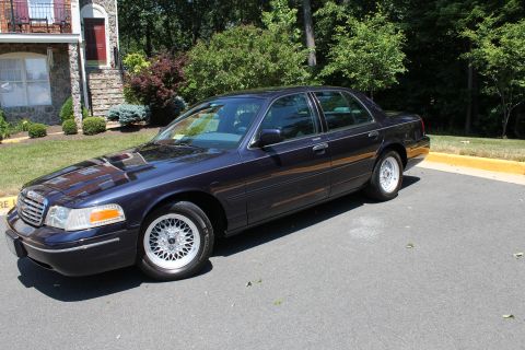 1999 Ford Crown Victoria - Dark blue 1999 Ford Crown Victoria sedan parked on asphalt with a building in the background.