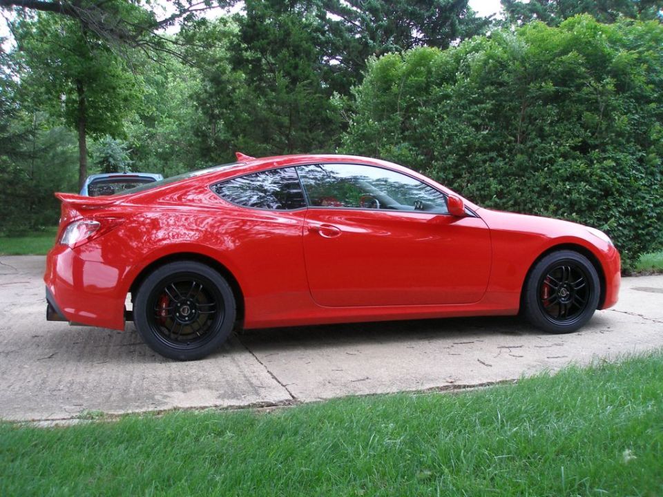 Red coupe parked on driveway, side view. Looks like a 2010 Hyundai Genesis