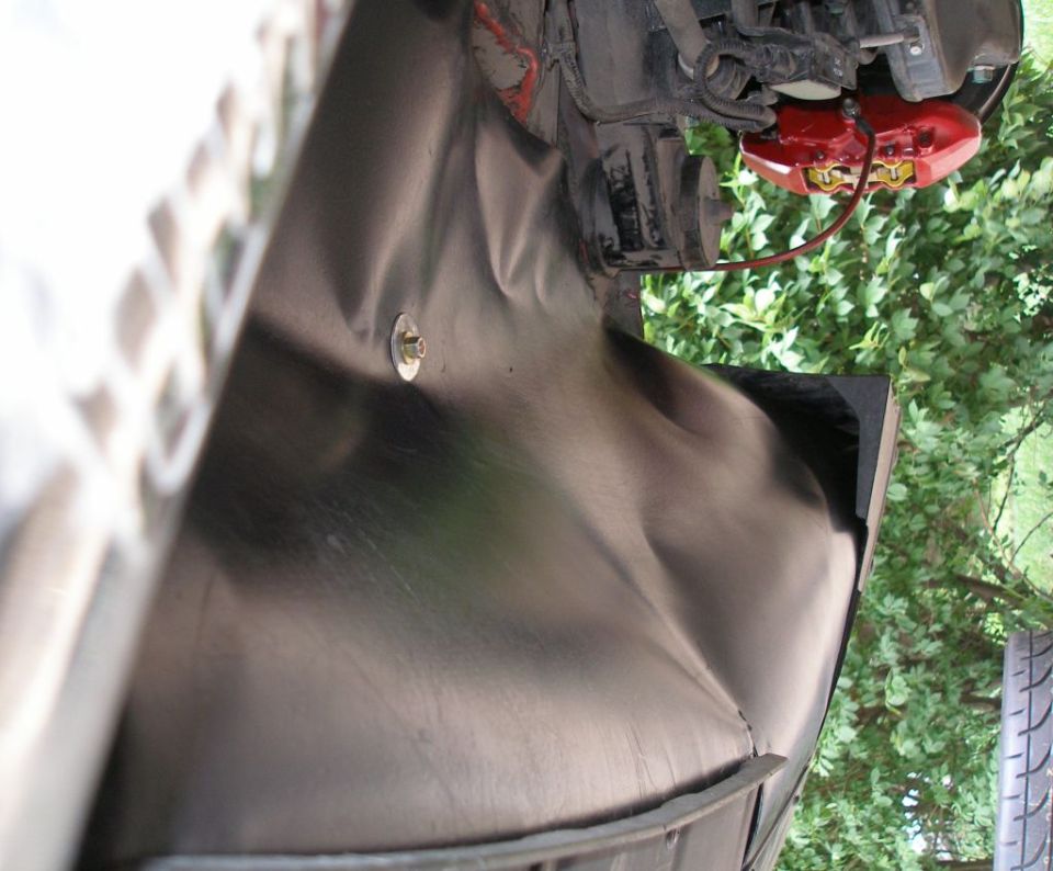 Black plastic wheel well liner with a visible bolt and red brake caliper in the background