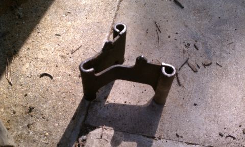 1990 Ford Bronco - A metal bracket with two U-shaped ends rests on a concrete surface.