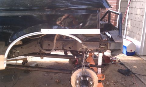 1990 Ford Bronco - The rear suspension and frame of a black SUV, likely a 1990 Ford Bronco, are visible as it is supported by jack stands.