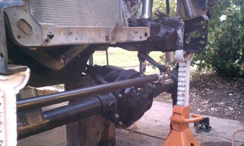 1990 Ford Bronco - Close-up of vehicle's front axle and suspension components, supported by jack stands.