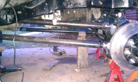 1990 Ford Bronco - Under-vehicle side view of a custom radius-arm/link suspension being fabricated, with two long bare-steel tubes running from frame-rail bra…