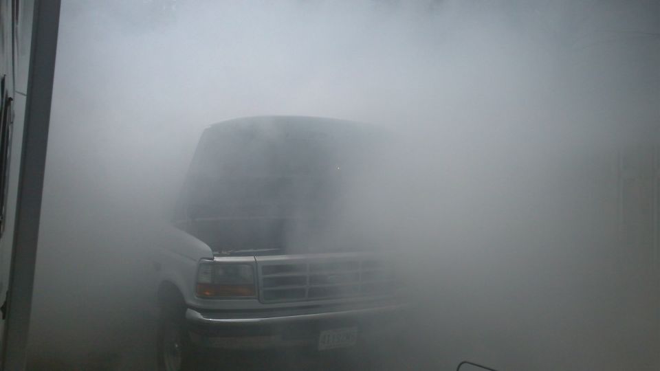 White Ford Bronco with hood open, obscured by smoke, front view