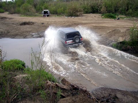 1989 Ford Bronco - A 1989 Ford Bronco splashes through a water crossing, with another vehicle visible in the background.