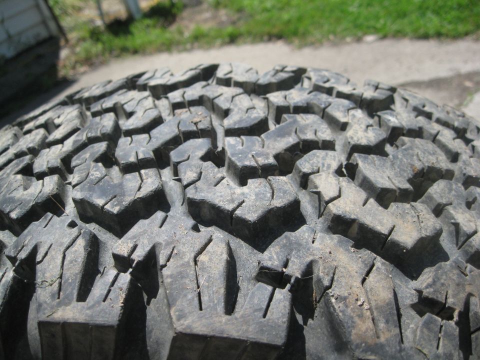Close-up of a worn off-road tire tread with mud. Supermotors.net logo visible