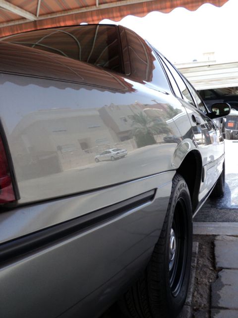2001 Mercury Grand Marquis - The side of a silver sedan is shown, with reflections of buildings and another car visible on its polished surface.