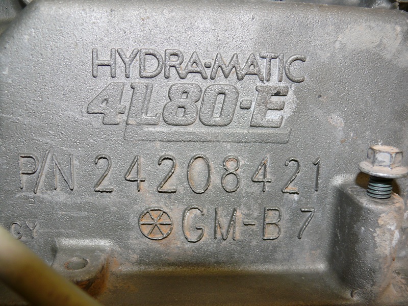 Close-up of a metal part with 'HYDRA-MATIC 4L80-E' and 'P/N 24208421 GM-B 7' stamped on it
