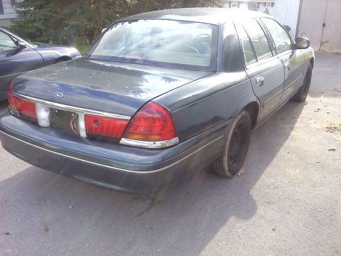 1998 Ford Crown Victoria - A dark green 1998 Ford Crown Victoria sedan is parked outdoors next to another vehicle.