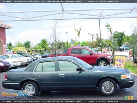 1998 Ford Crown Victoria - A dark green 1998 Ford Crown Victoria Police Interceptor is seen from the side, with other vehicles and a sale sign in the background.