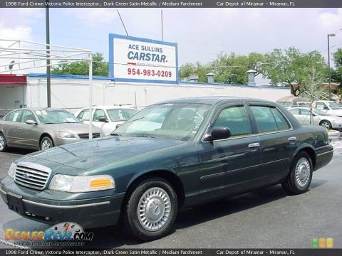 1998 Ford Crown Victoria - A dark green 1998 Ford Crown Victoria police interceptor is parked in front of a car dealership.