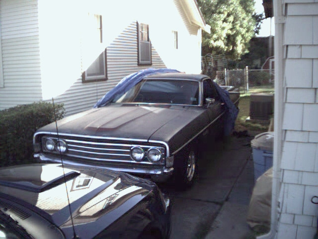 Dark vintage Ford Ranchero from front 3/4 angle in driveway with blue tarp on roof