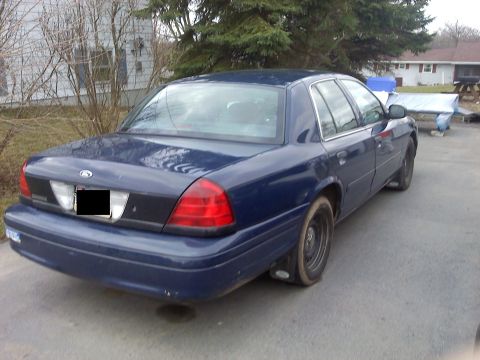 2002 Ford Crown Victoria - This sedan is parked outside a house with trees and other vehicles in the background.