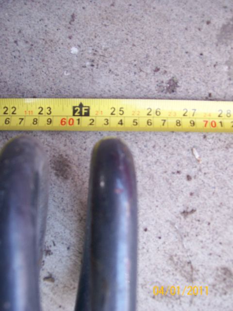 1970 Ford Bronco - A close-up view of two dark metal pipes, with a measuring tape indicating their size.