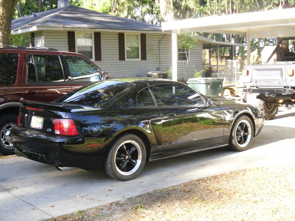 Black Ford Mustang parked next to a maroon SUV and a light-colored truck