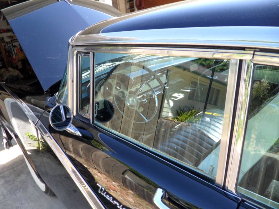 Black 1956 Ford Fairlane interior with chrome steering wheel and quilted seats, seen from the side