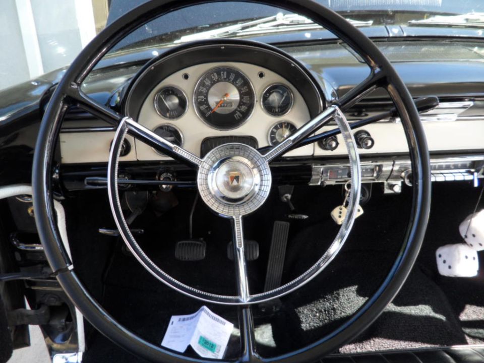 1956 Ford Fairlane interior showing steering wheel, dashboard gauges, and pedals